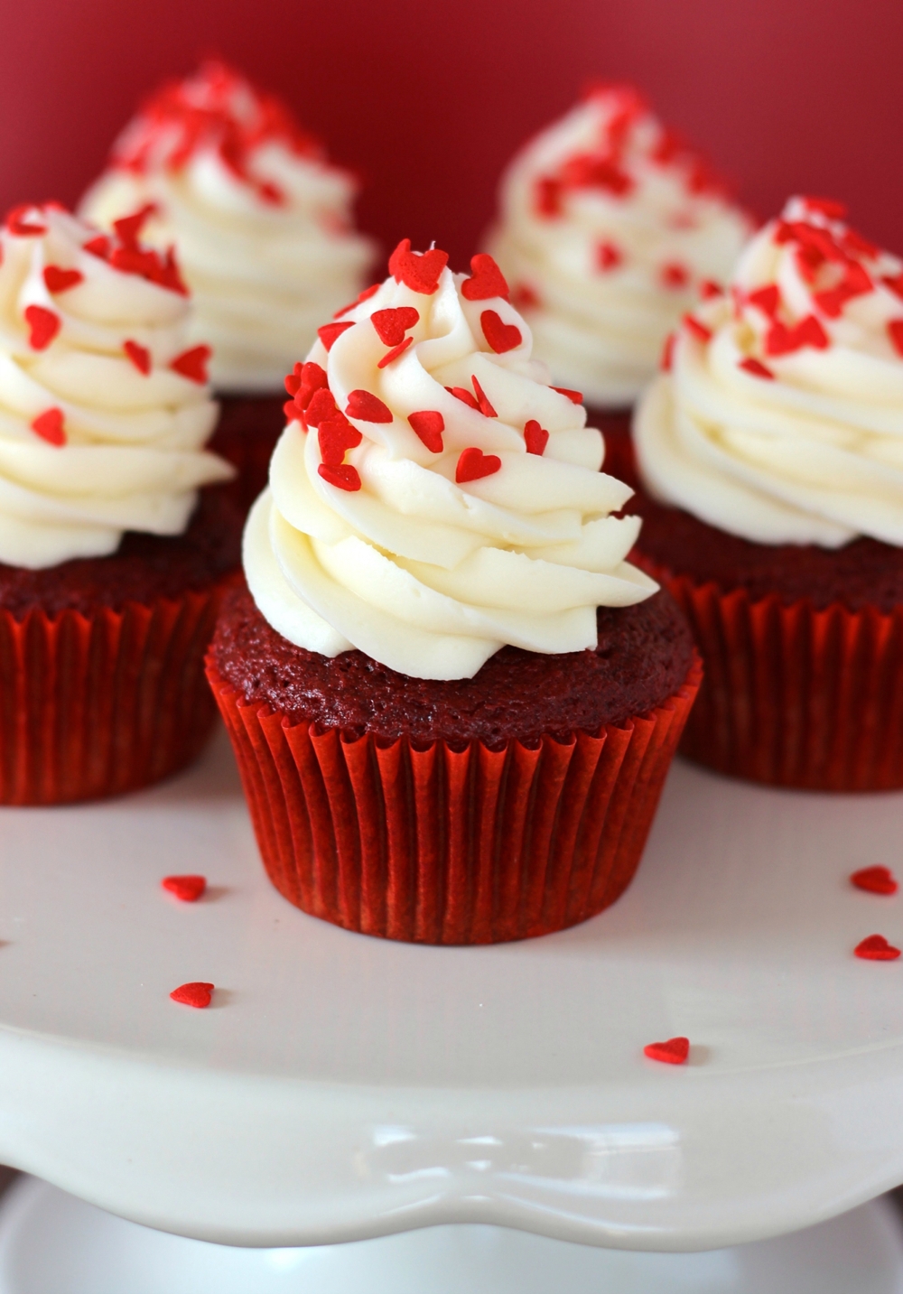 five red velvet cupcakes on a white plate with red harts on top of there white topping